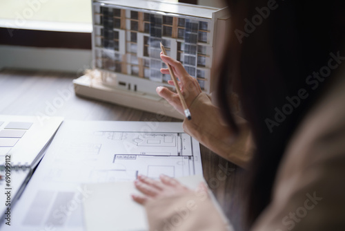 Female architect looking on building model and designing architecture interior project on blueprint photo