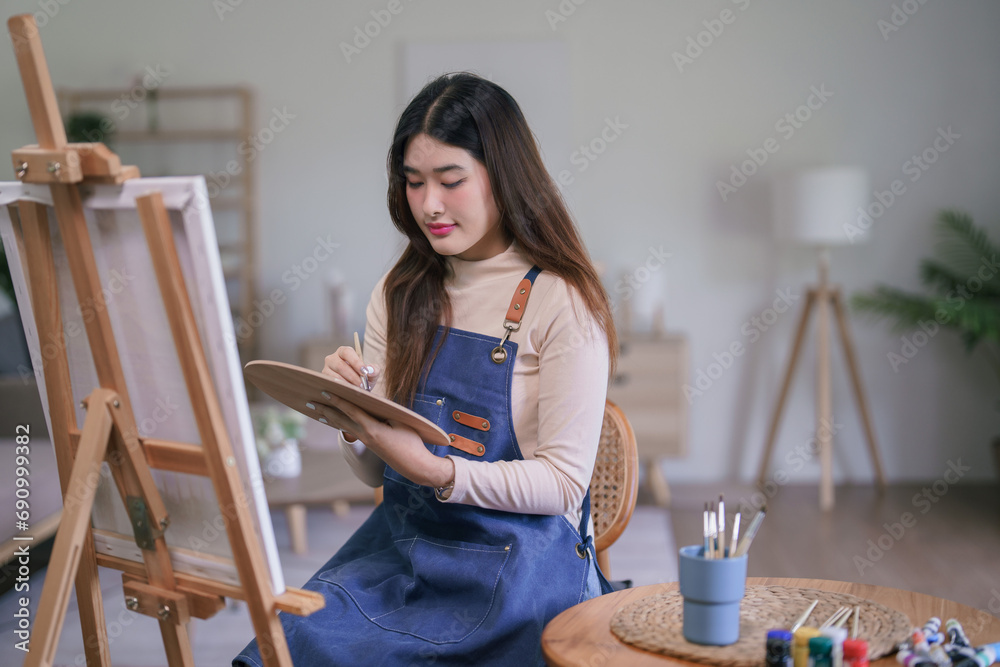 Young asian female artist using paintbrush with color palette to create painting artwork on canvas Young asian female artist using paintbrush with color palette to create painting artwork on canvas
