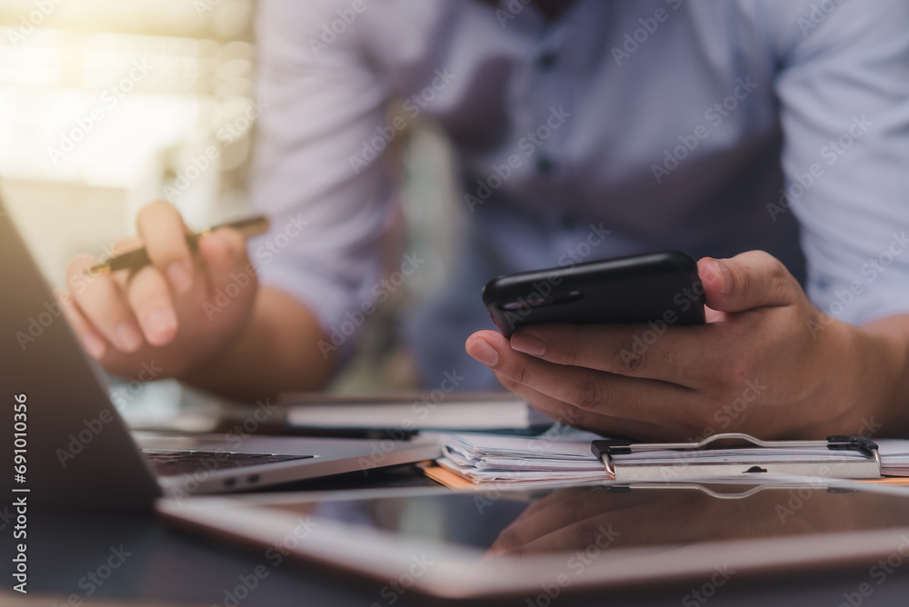 Fototapeta premium Businessman hand holding mobile smartphone on a table with a laptop at office.....