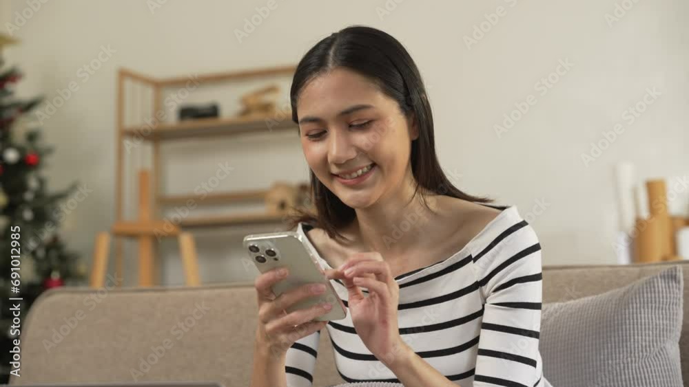 young Asian woman confidently using a smartphone, texting, chat with friends and video call sitting on a beige couch with a white cushion. young Asian woman confidently using a smartphone, texting, chat with friends and video call sitting on a beige couch with a white cushion.