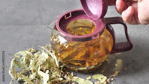 A person is holding a herbal tea teapot with linden tea in it,
