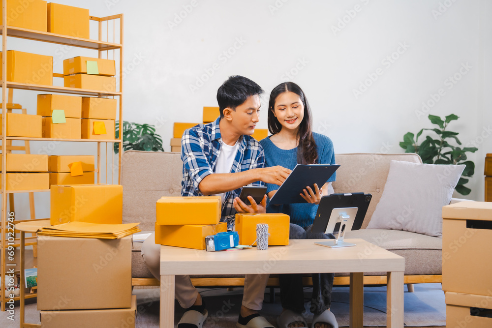 Asian people SME business woman and man couple joyfully showcasing products during a live stream in a room filled with packing boxes. Asian people SME business woman and man couple joyfully showcasing products during a live stream in a room filled with packing boxes.