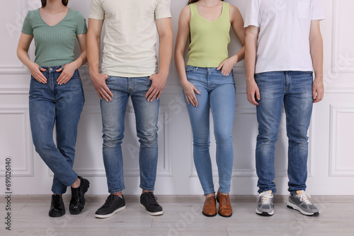 Group of people in stylish jeans near white wall indoors, closeup photo