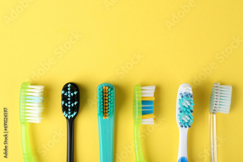 Different toothbrushes on yellow background, flat lay. Space for text