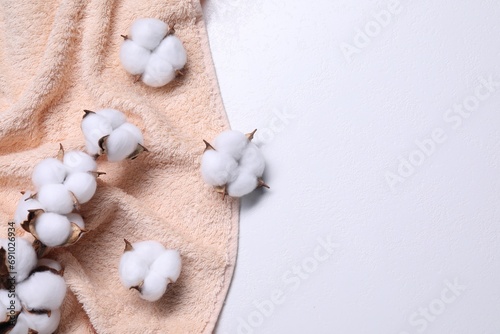 Cotton branch with fluffy flowers and beige terry towel on white background, top view. Space for text