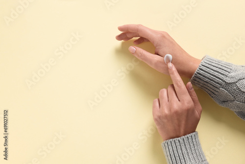 Woman applying cosmetic cream onto hand on beige background, top view. Space for text photo