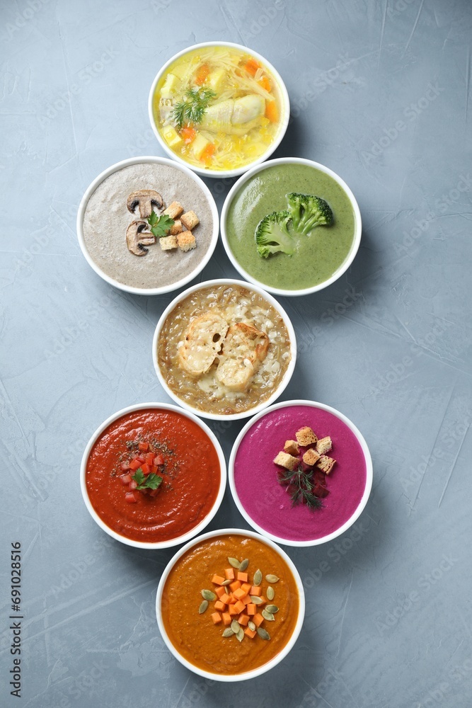 Tasty broth and different cream soups in bowls on gray table, flat lay Tasty broth and different cream soups in bowls on gray table, flat lay