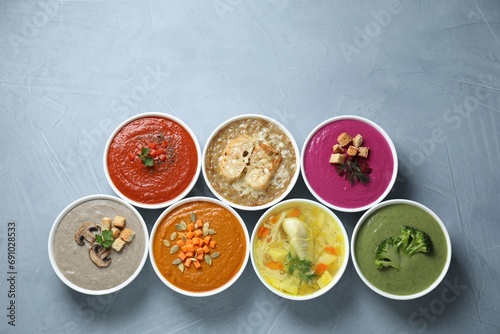 Tasty broth and different cream soups in bowls on gray table, flat lay