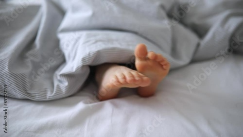 Little child's feet in bed covered with blanket photo