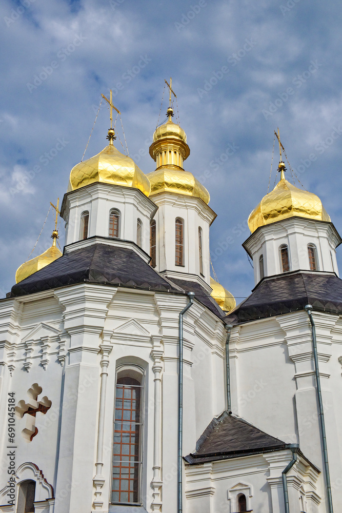 Catherine's Church in Chernihiv, Ukraine, a resplendent white church adorned with golden domes, stands majestically against the canvas of a serene blue sky with drifting clouds.