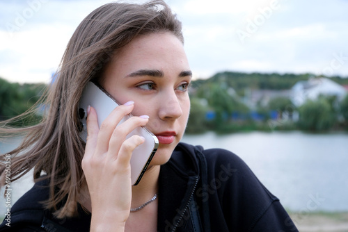 Happy girl standing in the park and chatting on cellphone close-up face white phone against the backdrop of a pond light smile talk a lot 60 frames per second 4K