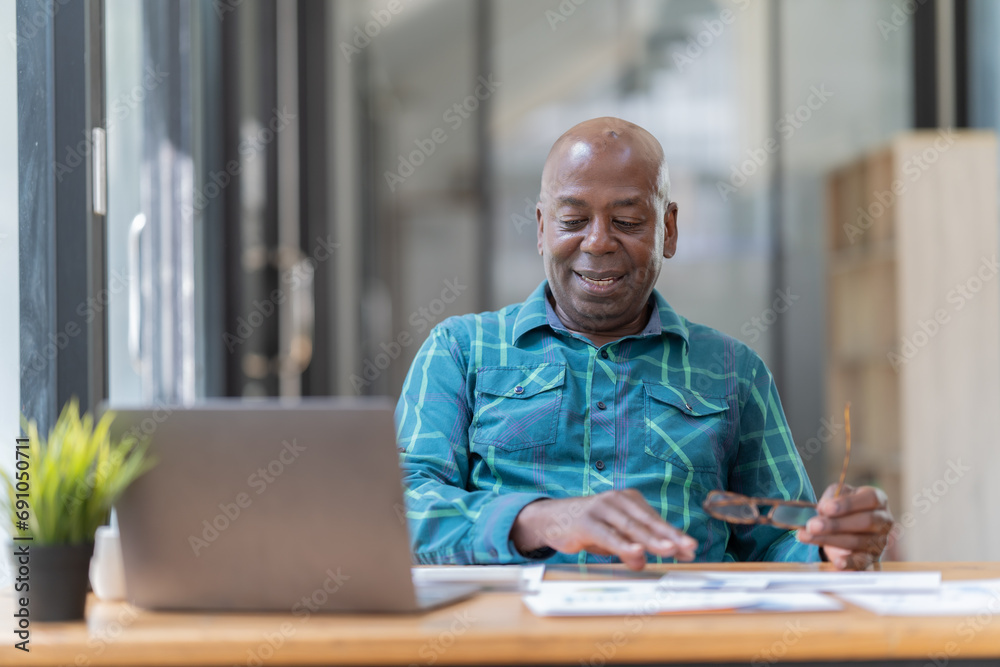 Naklejka premium Portrait of happy African American small business owner. Millennial black smiling, sitting and using the laptop, and holding a cup of coffee work in modern office.