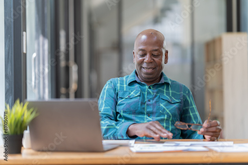 Portrait of happy African American small business owner. Millennial black smiling, sitting and using the laptop, and holding a cup of coffee work in modern office.