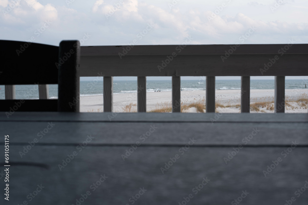 Unique perspective of a beach scene framed into small sections by deck railing.  Unrecognizable people fishing in the surf. copy space.