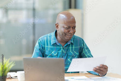 Portrait of happy African American small business owner. Millennial black smiling, sitting and using the laptop, and holding a cup of coffee work in modern office.