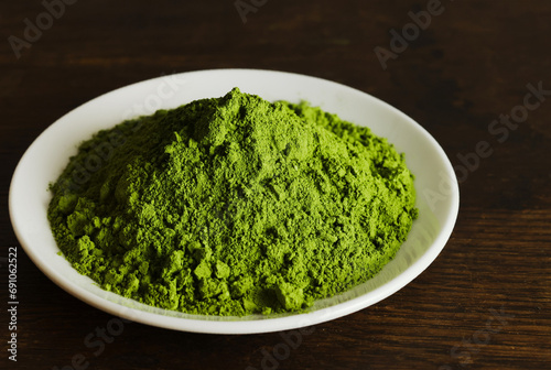 Closeup top view heap of dry organic matcha green tea powder in white plate isolated on dark wooden background.