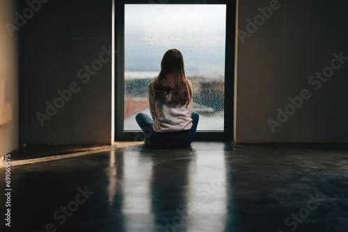 Lonely young woman feeling depressed and stressed sitting alone, looking thru rainy window