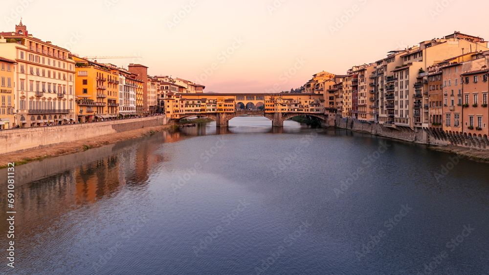 Arno river embankment with Ponte Vecchio bridge and buildings of old city at sunset, Florence, Italy
