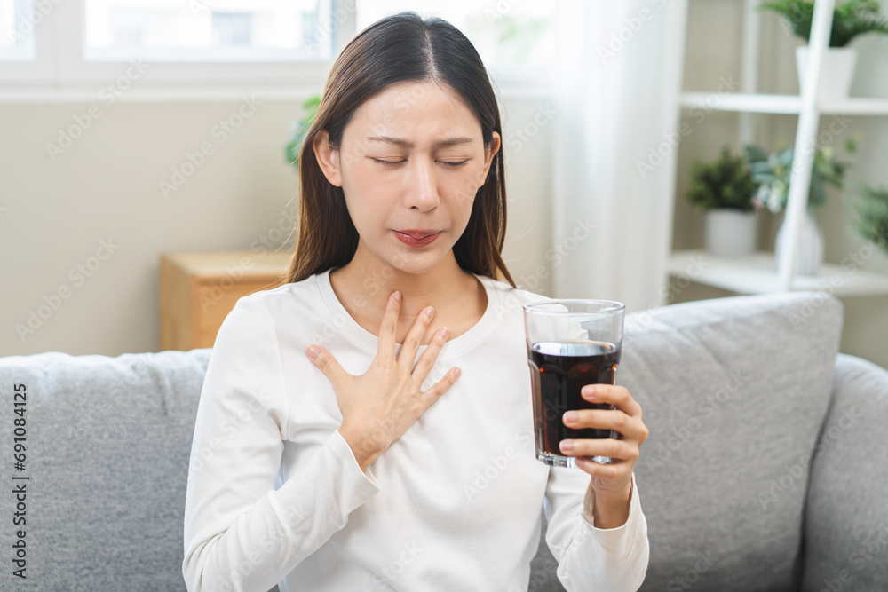 Acid reflux disease, suffer asian young woman, girl hand holding a glass of cola, have symptom gastroesophageal, heartburn pain on chest when drinking sparkling, soft water. Healthcare medical concept Acid reflux disease, suffer asian young woman, girl hand holding a glass of cola, have symptom gastroesophageal, heartburn pain on chest when drinking sparkling, soft water. Healthcare medical concept