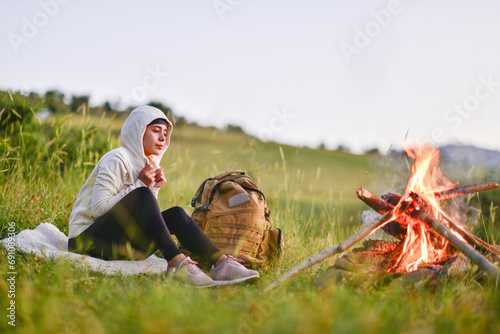 young lady camping at the foot of the mountain, watching the sunset in front of the fire