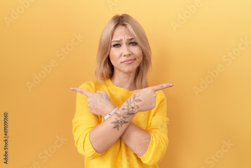 Young caucasian woman wearing yellow sweater pointing to both sides with fingers, different direction disagree photo