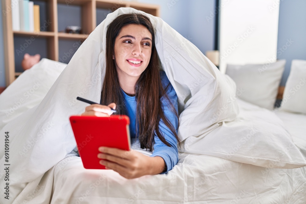 Young beautiful hispanic woman using touchpad lying on bed at bedroom Young beautiful hispanic woman using touchpad lying on bed at bedroom