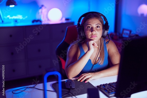 Young beautiful hispanic woman streamer sitting on table with relaxed expression at gaming room
