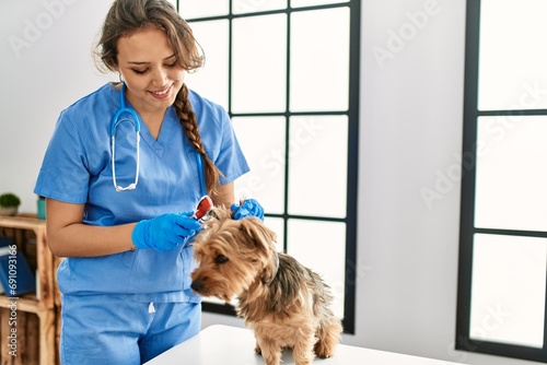 Young beautiful hispanic woman veterinarian examining dog with otoscope at home photo