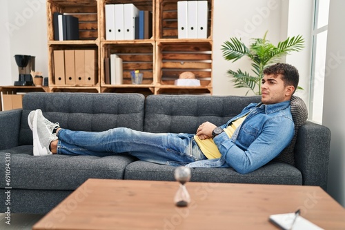 Young hispanic man patient lying on sofa speaking at psychology clinic