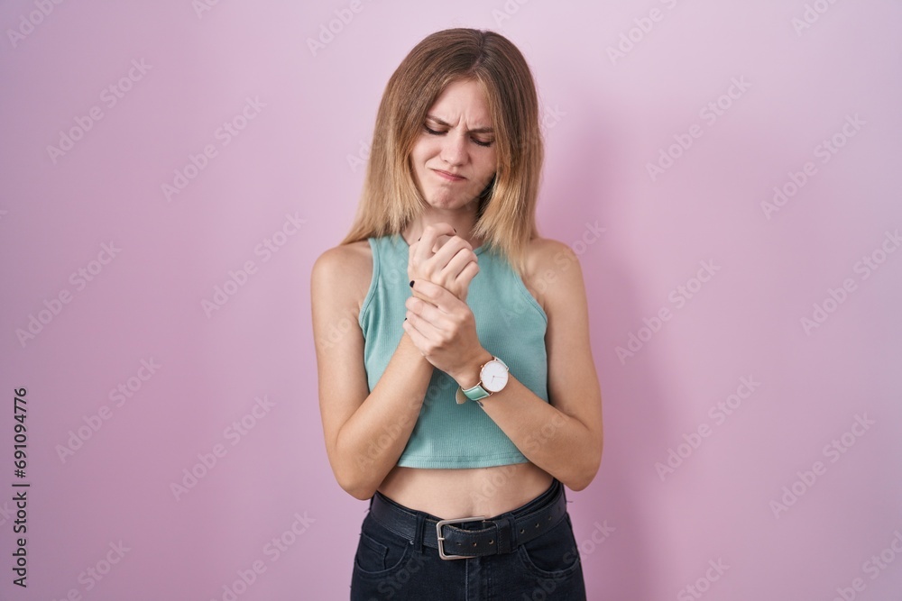 Blonde caucasian woman standing over pink background suffering pain on hands and fingers, arthritis inflammation Blonde caucasian woman standing over pink background suffering pain on hands and fingers, arthritis inflammation