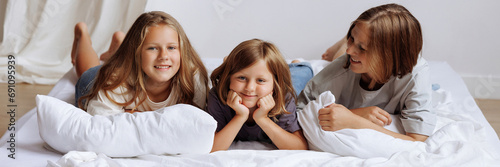 Sisters lying on a bed in their home  smmiling for the camera. Banner with copy space.