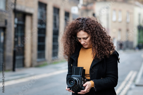 Mature female photographer using medium format analog film camera in the street. photo
