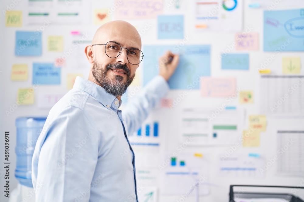 Young bald man business worker writing on wall paper at office