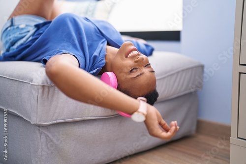 African american woman listening to music lying on sofa at home