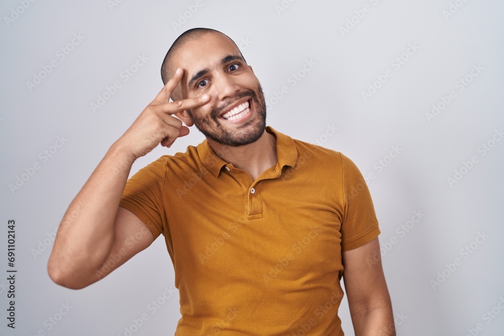 Hispanic man with beard standing over white background doing peace symbol with fingers over face, smiling cheerful showing victory Hispanic man with beard standing over white background doing peace symbol with fingers over face, smiling cheerful showing victory