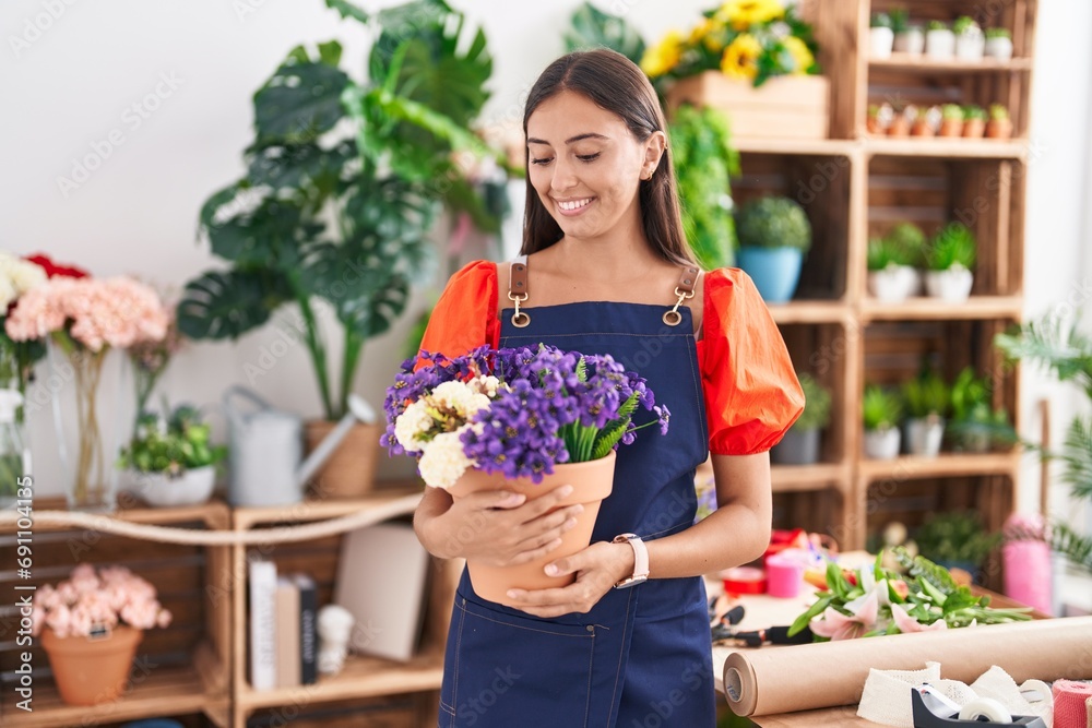 Young beautiful hispanic woman florist smiling confident holding plant at florist