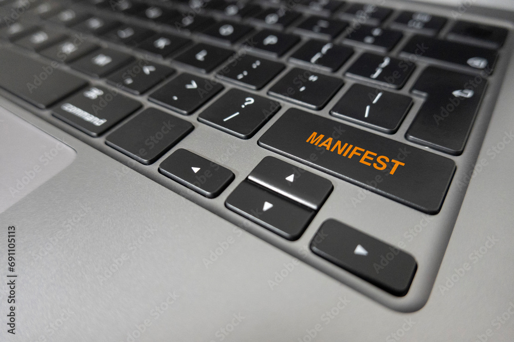 The word Manifest written on laptop keyboard in orange text extreme closeup