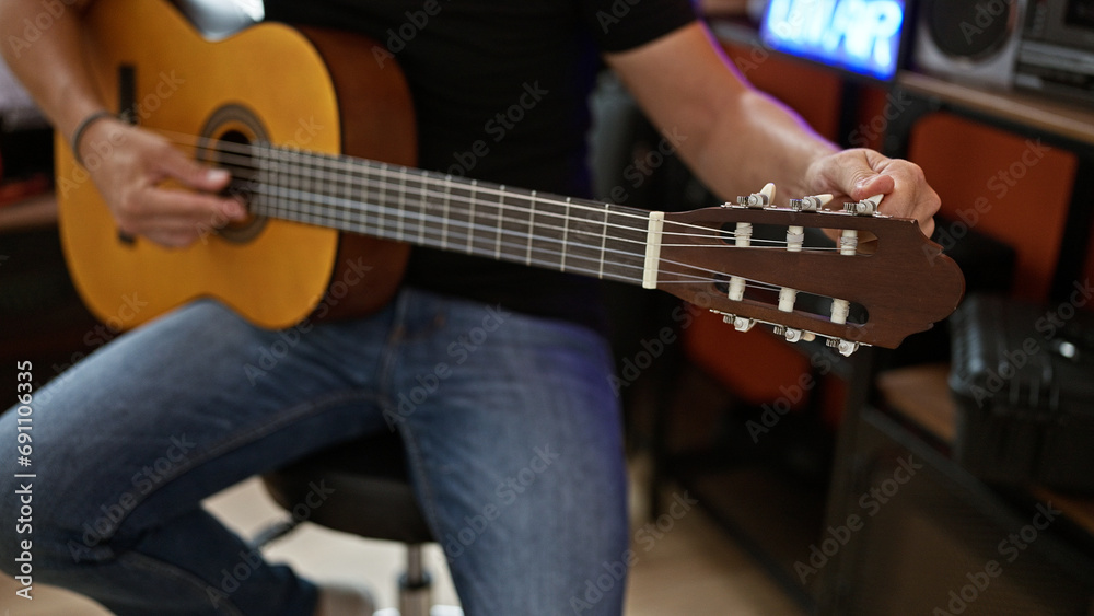 Obraz premium Young hispanic man musician playing classical guitar at music studio