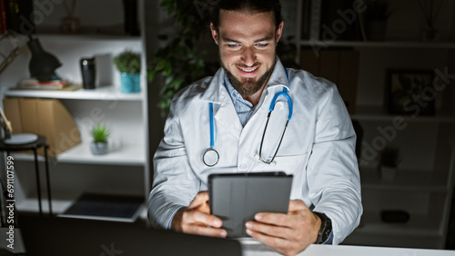 фотографія Young hispanic man doctor using touchpad working at the clinic