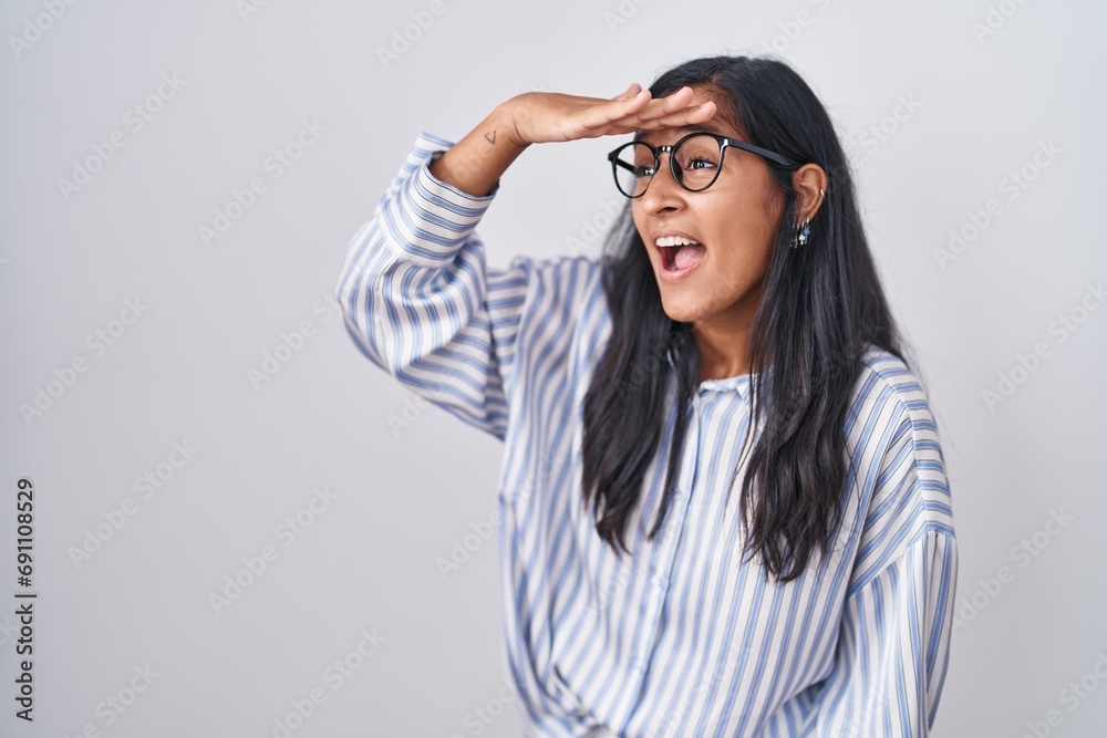Young hispanic woman wearing glasses very happy and smiling looking far away with hand over head. searching concept. Young hispanic woman wearing glasses very happy and smiling looking far away with hand over head. searching concept.