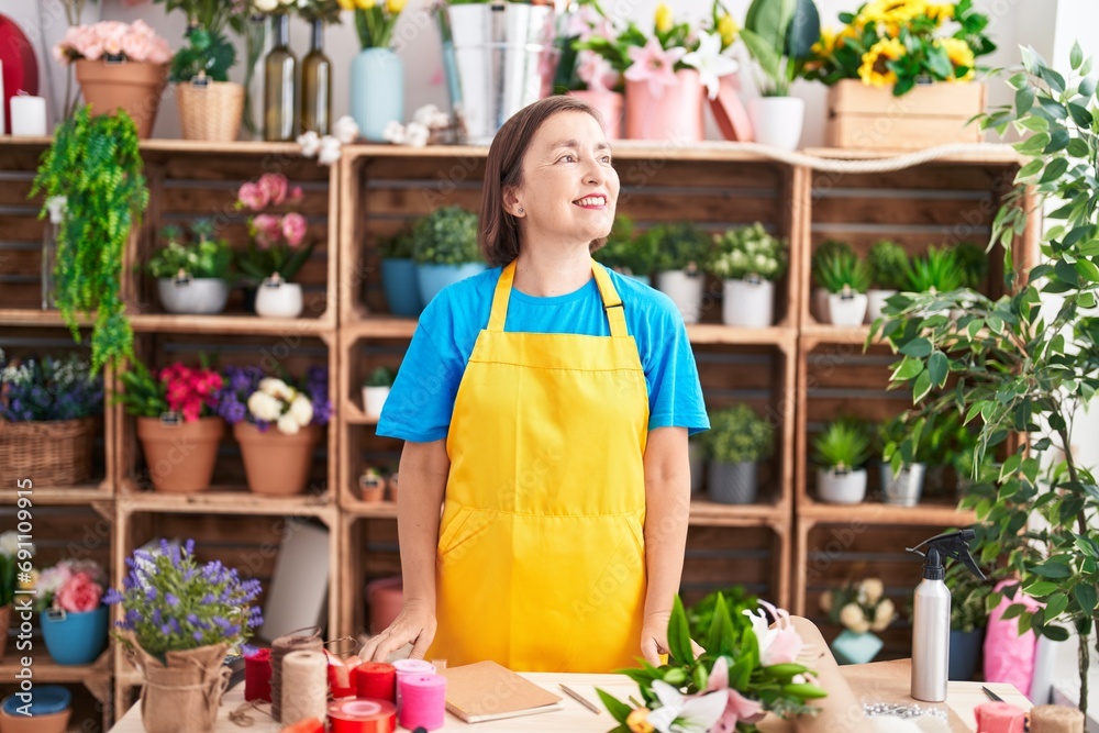 Middle age hispanic woman working at florist shop looking to side, relax profile pose with natural face and confident smile.