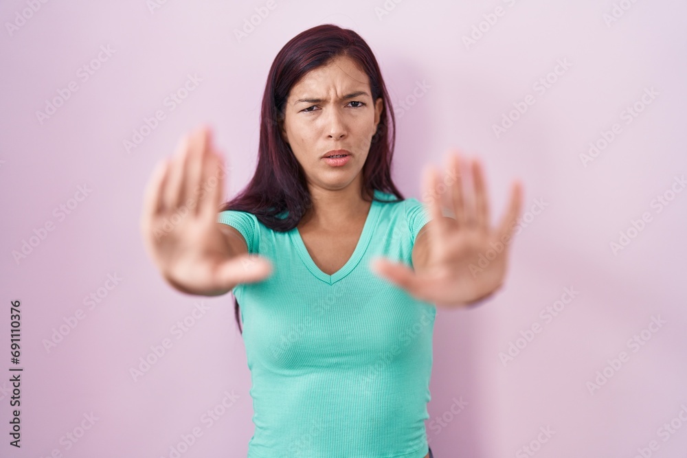 Young hispanic woman standing over pink background doing stop gesture with hands palms, angry and frustration expression Young hispanic woman standing over pink background doing stop gesture with hands palms, angry and frustration expression