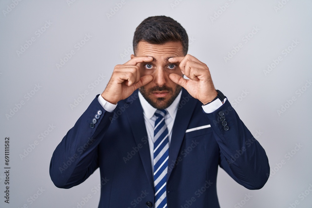 Handsome hispanic man wearing suit and tie trying to open eyes with fingers, sleepy and tired for morning fatigue Handsome hispanic man wearing suit and tie trying to open eyes with fingers, sleepy and tired for morning fatigue