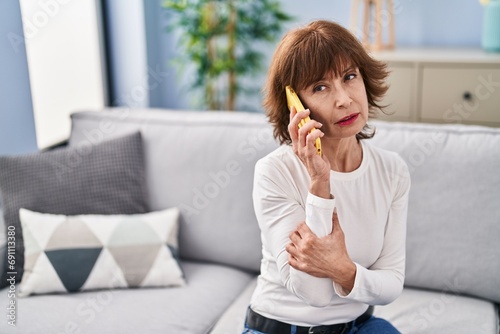 Middle age woman talking on smartphone with worried expression at home