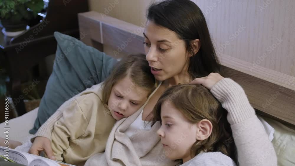 Mom is lying on the bed with her children, reading a bedtime story. Her son and daughter are happily listening to the stories