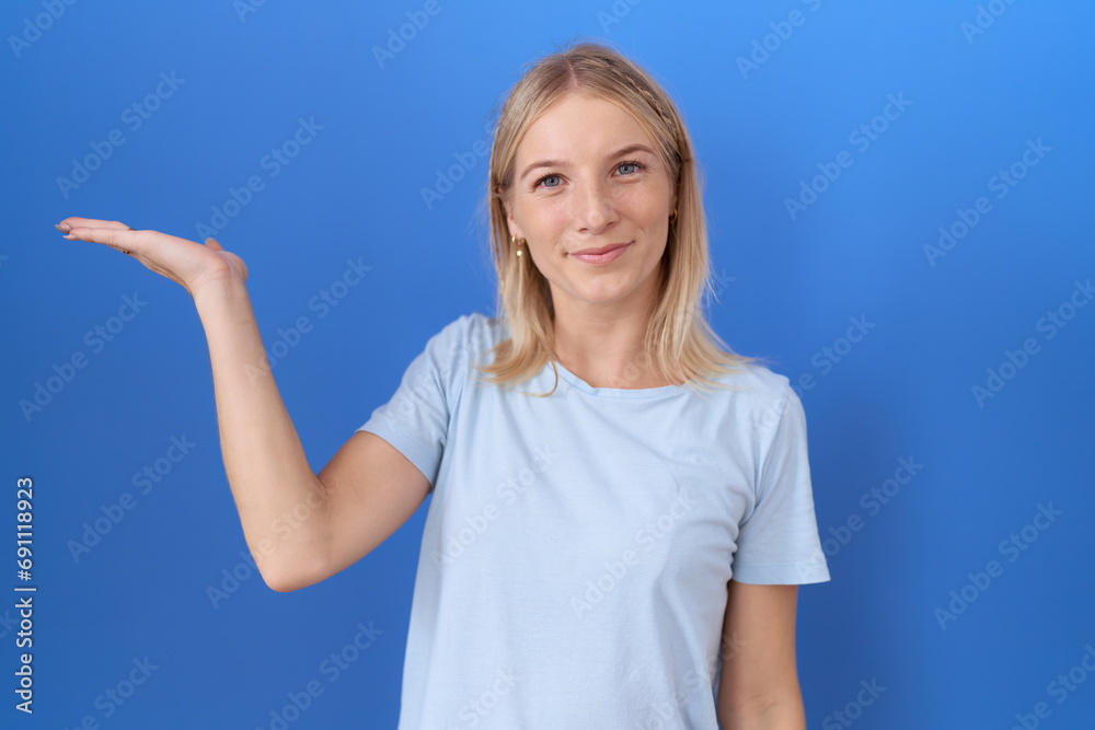 Fototapeta premium Young caucasian woman wearing casual blue t shirt smiling cheerful presenting and pointing with palm of hand looking at the camera.