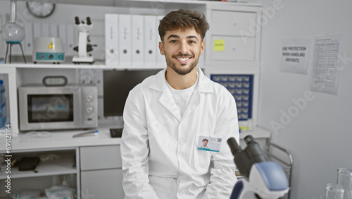Confident young arab man, a smiling scientist, dives into research in his lab, perfecting his craft with a microscope and immense passion for science