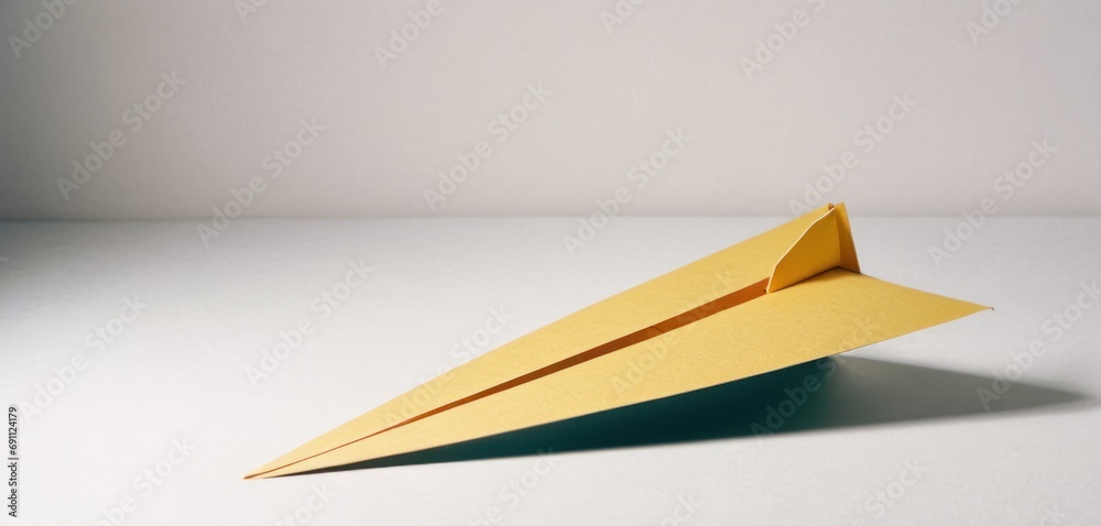 a yellow origami airplane sitting on top of a white table with a shadow on the wall behind it. a yellow origami airplane sitting on top of a white table with a shadow on the wall behind it.
