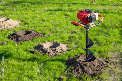 Obraz na płótnie Tool hand-held soil hole drilling machine or portable manual earth auger for prepare the soil for planting shrubs or trees in newly drilled hole on a green lawn