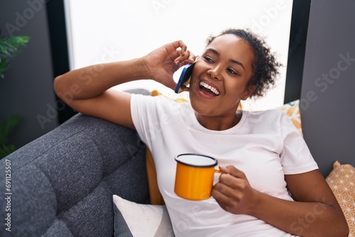 African american woman talking on smartphone drinking coffee at home